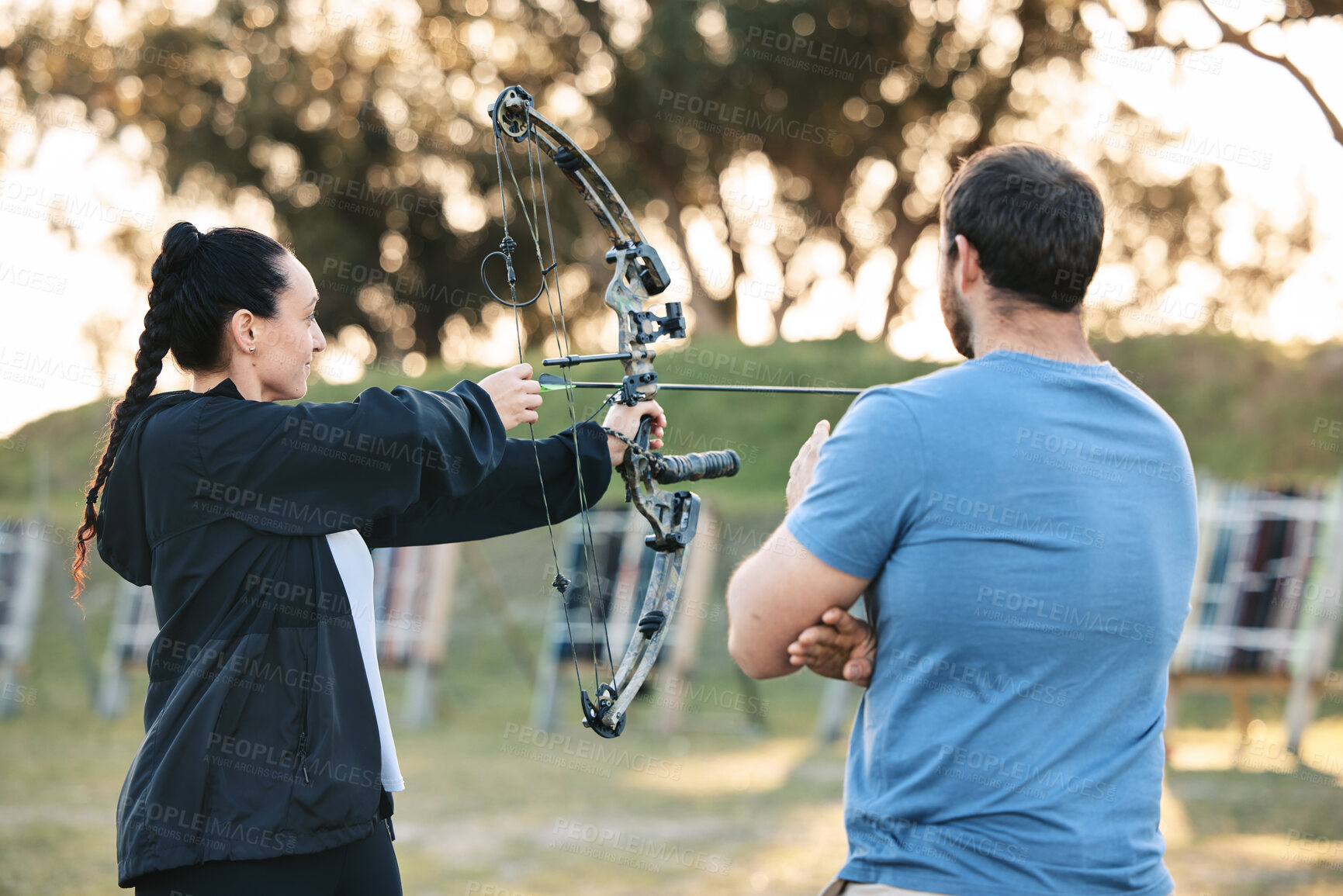 Buy stock photo Woman, archery and target training with an instructor on a field for hobby, aim and control. Arrow, practice and archer people together outdoor for hunting, precision and weapon, shooting competition