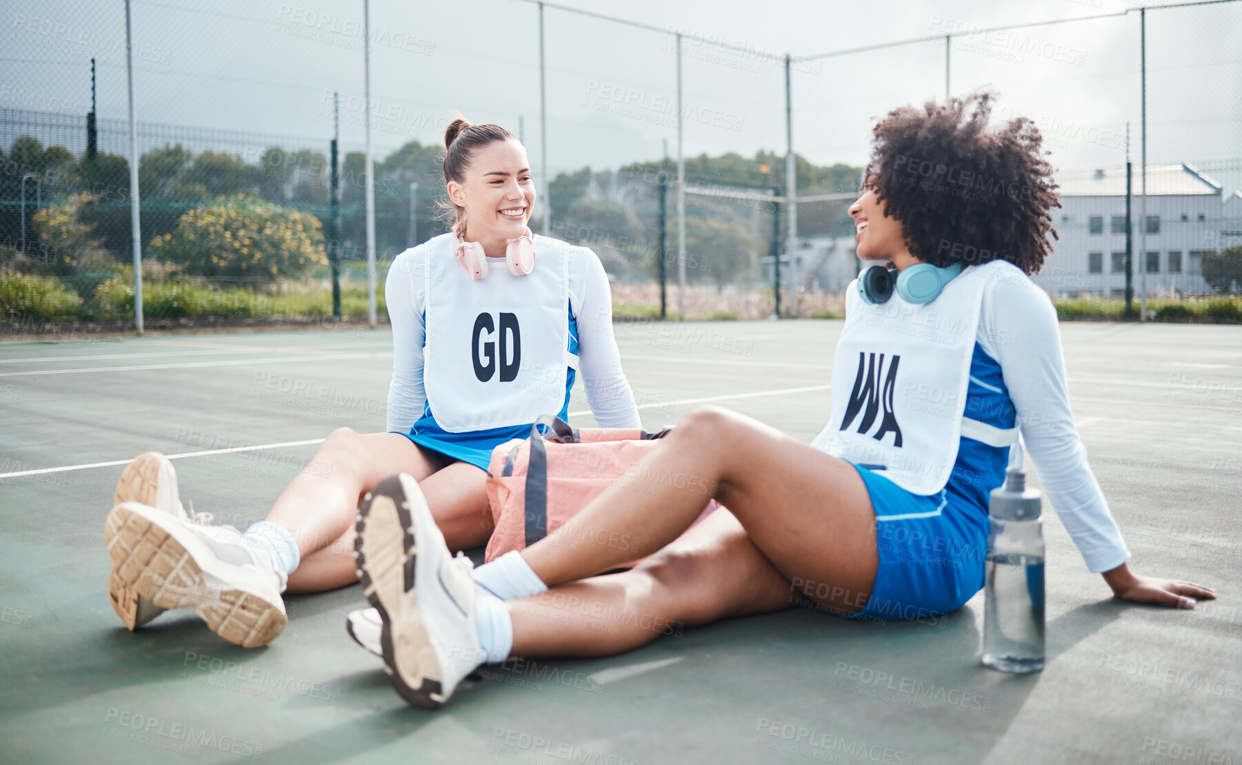 Buy stock photo Netball women, sport team and outdoor court exercise of students with diversity on a fitness break. Communication, athlete friends and wellness of a happy black woman with a friend sitting on ground