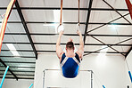 Man, acrobat and gymnast swinging on rings in fitness for practice, training or workout at gym. Professional male in gymnastics hanging on ring circles for athletics, acrobatics or strength exercise