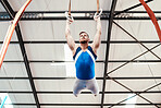 Man, acrobat and gymnastics swinging on rings in fitness for practice, training or workout at gym. Professional male gymnast hanging on ring circles for athletics, acrobatics or strength exercise