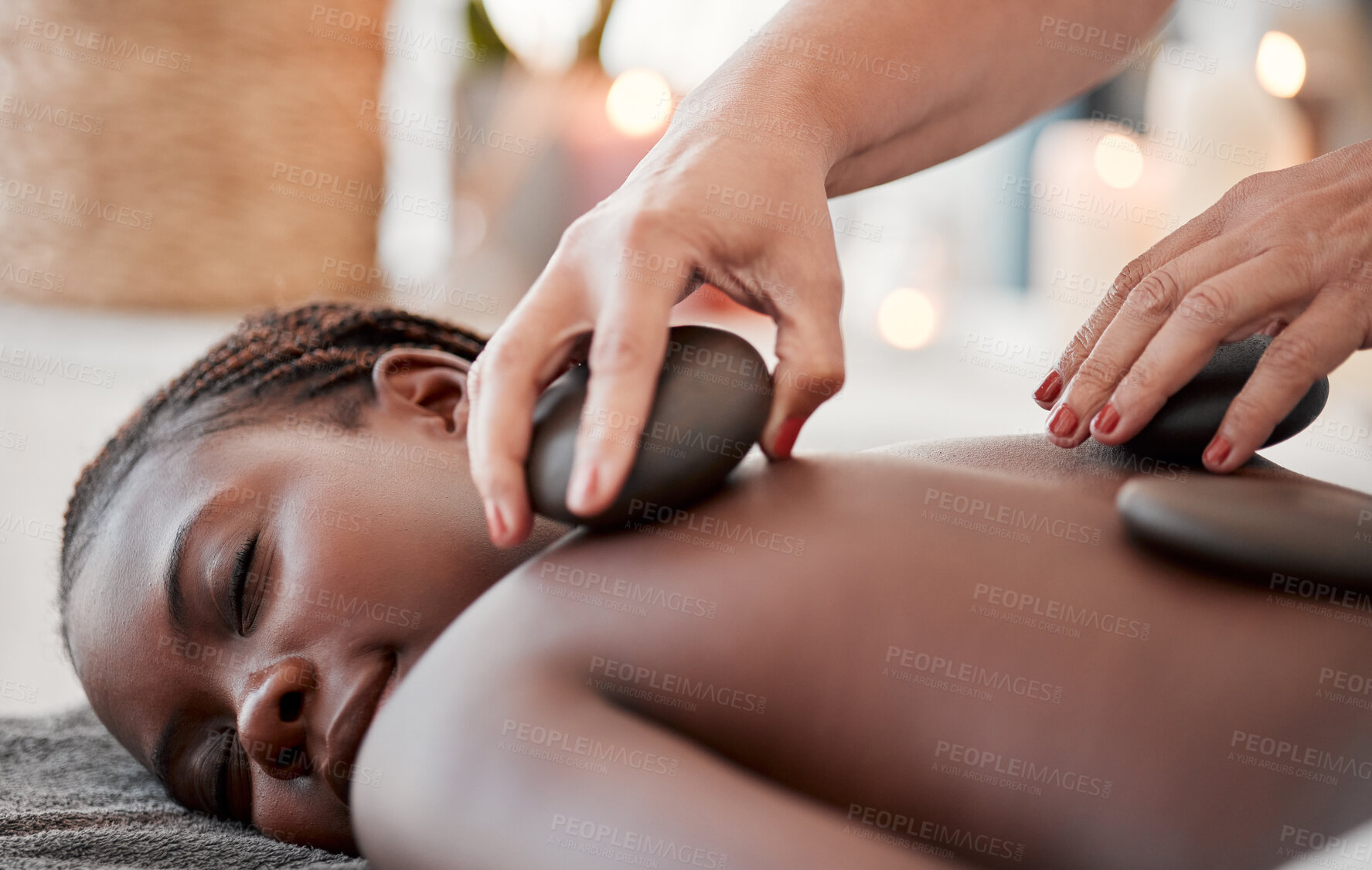 Buy stock photo Black woman, hot stone massage, spa and hands of masseuse, holistic and wellness, therapy and treatment. Health, peace of mind and rocks with zen, stress relief for people and back skin detox