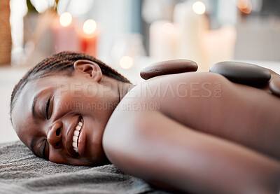 Buy stock photo Hot stone massage, black woman at spa with smile on face, holistic healing with physical therapy and back skin detox. Happy, content and zen with wellness at luxury resort, rocks and relax with glow