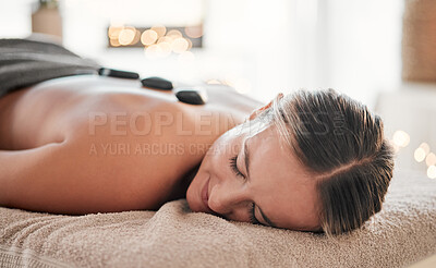 Buy stock photo Woman, stone and back on bed in spa treatment for relaxation, stress relief or massage at resort. Happy female relaxing with hot rocks in physical therapy for body healing, zen wellness or skincare