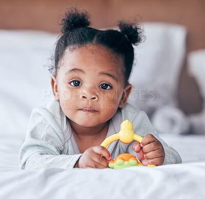 Buy stock photo Cute, portrait and baby with a toy on her bed playing and relaxing in her modern nursery. Childhood, playful and African girl infant or newborn playing with plastic object in her bedroom at her home.