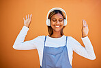 Music, dance and a young woman on an orange background in studio for freedom or fun. Radio, headphones and dancing with an attractive young female streaming subscription audio against a wall