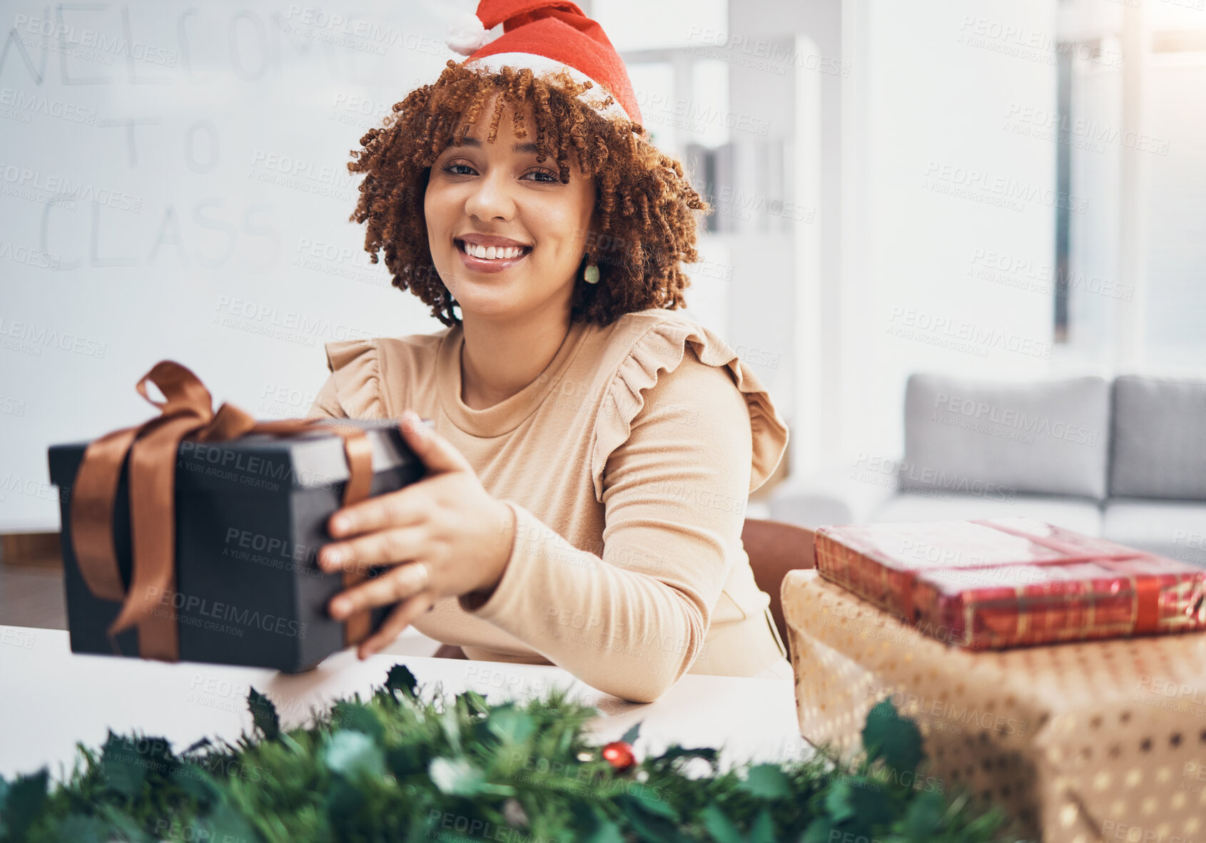 Buy stock photo Christmas, box and portrait with a black woman teacher giving a gift at her desk in a school in a classroom. December, holiday and present with a female educator holding a giftbox while feeling happy