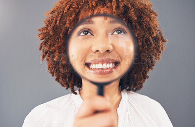 Buy stock photo Funny, smile and black woman with a magnifying glass on face isolated on a grey studio background. Happy, comic and facial zoom of a girl with a magnifier for comedy, happiness and discovery