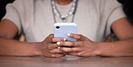 Black woman, hands and phone on table for social media, communication or chatting and texting. Hand of African American female browsing, typing or reading chat in networking on mobile smartphone app