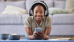 Black woman, student and phone with smile for elearning, education or entertainment by living room sofa at home. Happy African American female learner smiling on mobile smartphone lying on floor