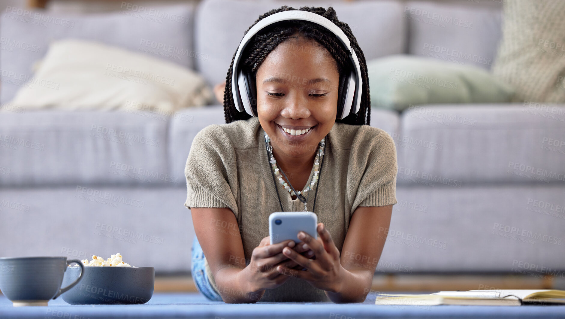 Buy stock photo Black woman, student and phone with smile for elearning, education or entertainment by living room sofa at home. Happy African American female learner smiling on mobile smartphone lying on floor