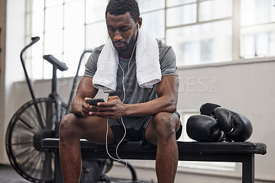 Buy stock photo Phone, music and fitness with a black man taking a break in a gym during his boxing workout. Exercise, social media or sports app with a male boxer or athlete tracking progress and resting on a bench