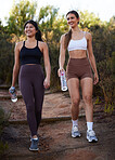 Fitness women or friends walking in nature with water bottle for workout, running and cardio training together. Diversity athlete, sports or runner people in woods with diet, body and wellness goals