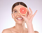 Woman, face and hand with grapefruit for skincare nutrition or healthy diet against gray studio background. Portrait of happy female smile with fruit for organic vitamin C facial or natural cosmetics