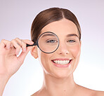 Magnifying glass, search or woman with beauty, skincare health or natural face grooming routine. Beauty, cosmetic or happy girl model with a lens for a wellness anti aging facial treatment in studio