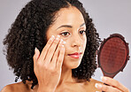 Face, skincare cream and black woman with mirror in studio isolated on a gray background. Dermatology cosmetics, reflection and female model with lotion, creme or moisturizer product for skin health.