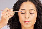 Face, makeup and black woman with eyeshadow brush in studio isolated on a gray background. Eyes closed, cosmetics and young female model with facial tool for beauty aesthetics, skincare and wellness.