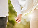 Couple holding hands in park for love, care and save the date marriage commitment together. Closeup hand of man, woman and walking in nature, garden and sunshine for relax, trust and support partner