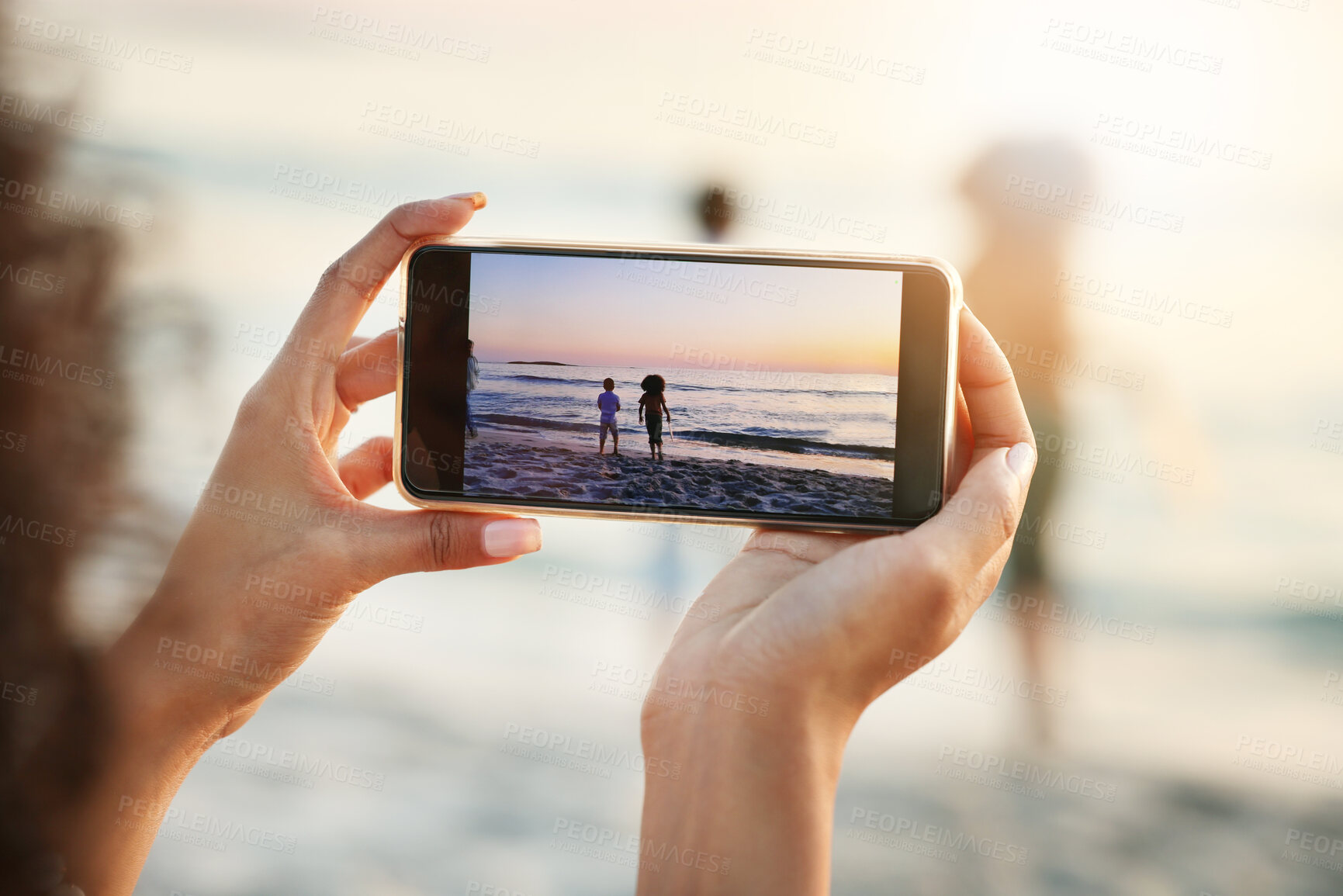 Buy stock photo Phone, photograph and beach with a woman in nature, recording her playing kids by the ocean outdoor. Mobile, family and sunset with a parent taking a picture of her kids on the sand at the sea