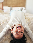 Portrait, child laughing and upside down on bed in bedroom home, having fun and smiling. Comic, smile and happy kid or girl laugh at funny joke, comedy or humor while relaxing and enjoying time alone