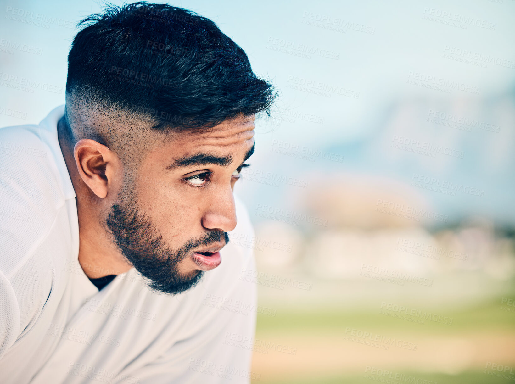 Buy stock photo Tired, breathing and sports man at a field for training, break and breathing exercise on blurred background. Athletic, sports and indian guy stop to breathe after exercise, workout or match practice