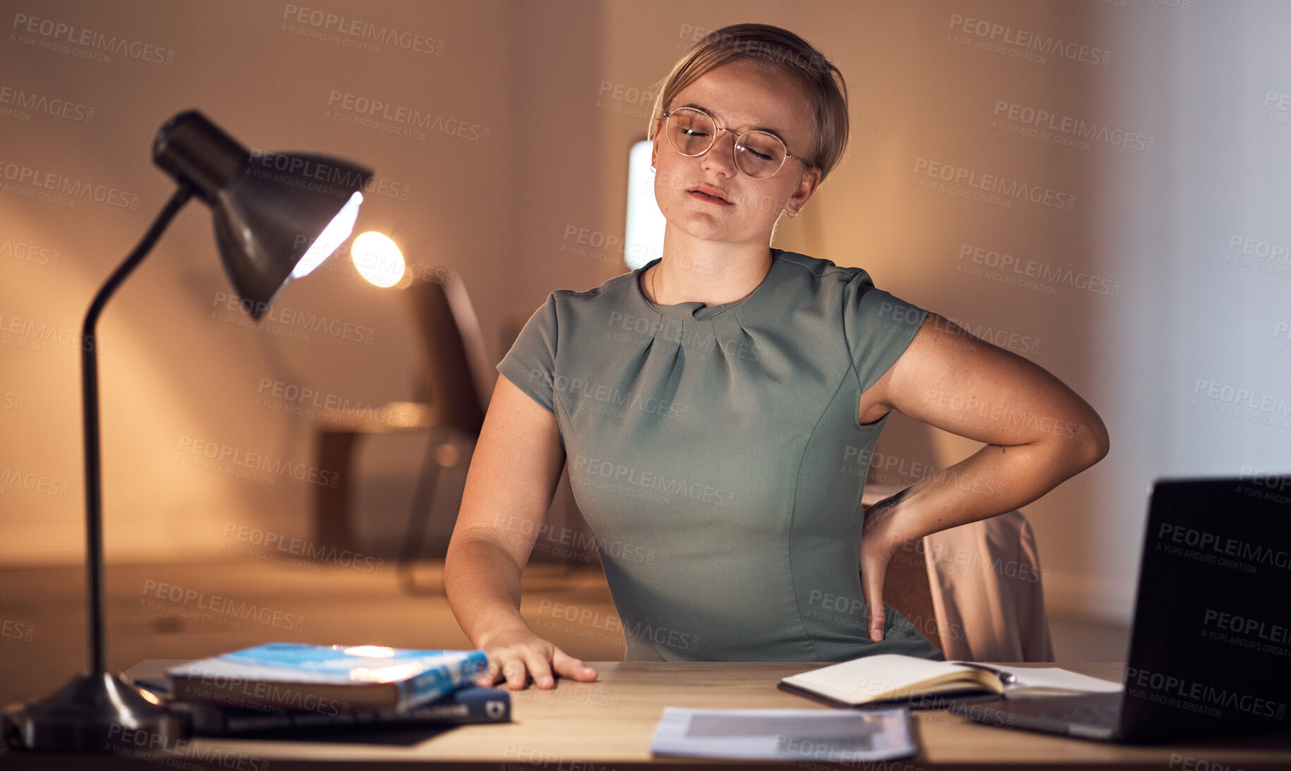 Buy stock photo Woman, office and night with back pain, burnout and stress at desk for overtime, fatigue and tired. Young corporate executive, manager and muscle strain in dark workplace, frustrated and exhausted