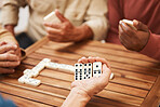 Hands, dominoes and friends in board games on wooden table for fun activity, social bonding or gathering. Hand of domino player holding rectangle number blocks playing with group for entertainment