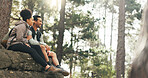 Nature, hiking and a couple relax on adventure trail in forest and sitting on a rock. Health, happy man and woman pointing at natural landscape while relaxing in woods with trees, fitness and freedom