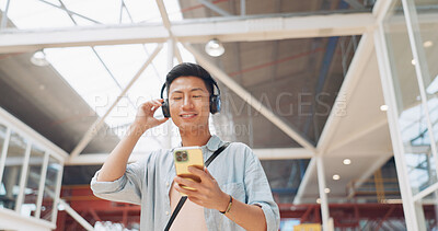 Phone, music headphones and Asian man walking in mall streaming podcast or radio. Technology, travel and happy male listening to song, audio sound or playlist on mobile smartphone in urban building.