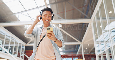 Asian man, phone and headphones for listening to music and dancing while walking in creative office with smile, happiness and positive mindset. Male entrepreneur during travel with network connection
