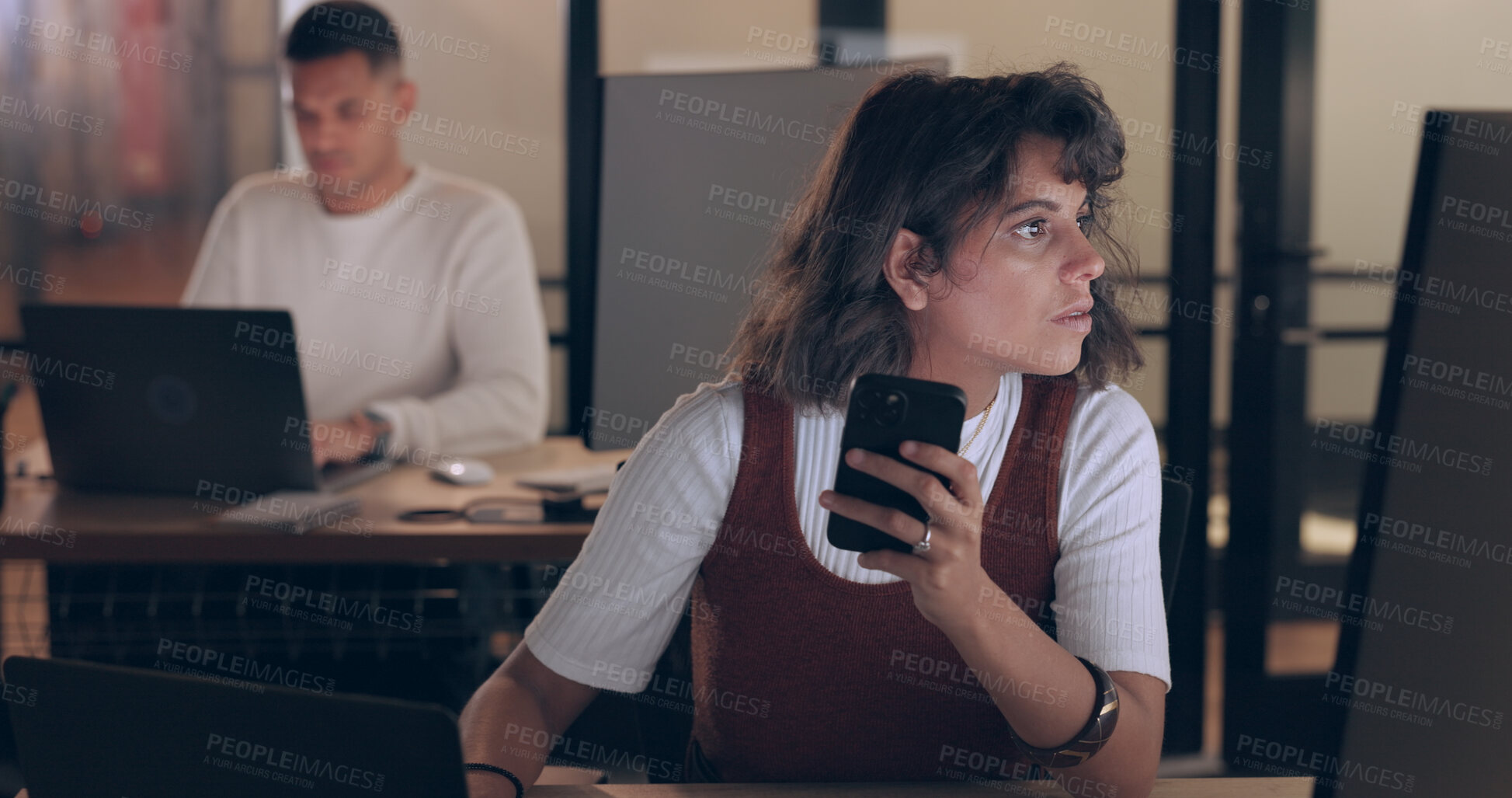 Buy stock photo Phone, computer and business woman in office at night, reading email and research app on deadline. Smartphone, focus and serious professional designer on internet, creative and typing in startup.