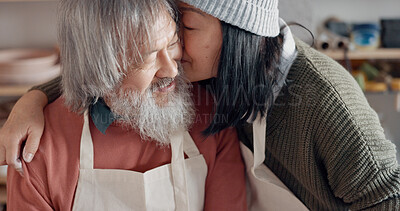 Pottery, creative and senior couple talking about art with hug and kiss together in a studio class. Elderly Asian man and woman hugging with love while learning and working with clay on a date