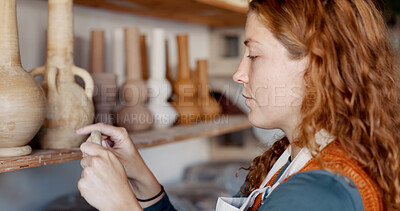 Buy stock photo Pottery, art and woman artist in workshop by a shelf for clay products in small business. Creative, mud design and young female sculptor checking or manufacturing ceramic handicraft goods in a studio