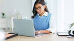 Young woman happily typing on laptop in neat white office doing business. Professional female is attractive and formal with work equipment and stationery around her. Busy emailing or messaging