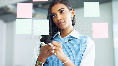 Young business woman brainstorming and planning a mind map while writing ideas on sticky notes on a glass wall in an office. Focused designer analyzing a marketing strategy and solutions for projects