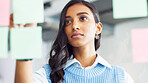 Young business woman brainstorming and planning a mind map with ideas on sticky notes on a glass wall in an office. One focused designer thinking while analyzing a marketing strategy with solutions