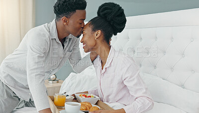 Breakfast in bed, love and black couple being romantic on their honeymoon, birthday or anniversary in a hotel room. Happy man kissing woman on head to express love and care while bonding in bedroom