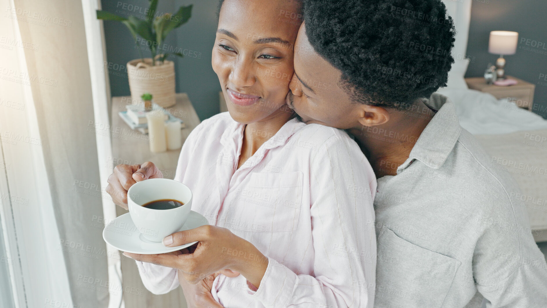 Buy stock photo Couple, kiss and coffee in the morning for love, happiness and care, watch and view from window in bedroom of home. 
Romance, black woman and man in room embrace for commitment and healthy marriage
