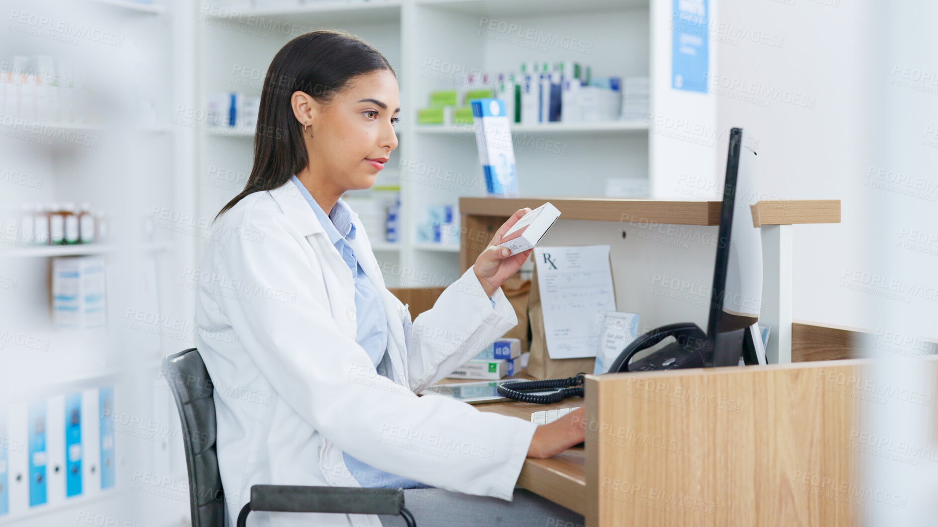 Buy stock photo Young pharmacist working on computer at a pharmacy counter. Woman using technology to access drug database, does inventory checkup and dispensing online medicine prescriptions in a drugstore.