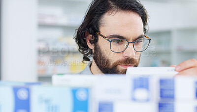 Man with glasses choosing medication on a shelf in a pharmacy. Customer with glasses browsing in aisle in a drugstore and finding what he needs before heading to the checkout with his vitamins