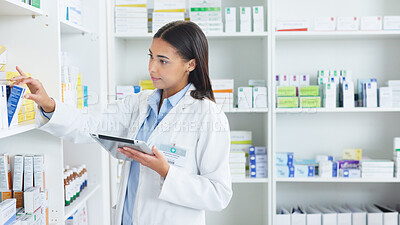 A young female pharmacist stocktaking in a dispensary using a tablet. Doctor preparing prescriptions and medication at clinic or pharmacy. Healthcare professional sorting medicine with digital device