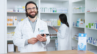Portrait of a cheerful and friendly pharmacist using a digital tablet to check inventory or online orders in a chemist. Young caucasian man using pharma app to do research on medication in a pharmacy