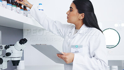 Medical researcher checking bottles with chemicals inside a modern science lab. Young focused scientist or pharmacist looking at hazardous and dangerous inventory while writing notes in a pharmacy