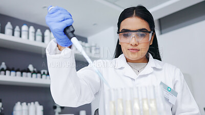 Female scientist experimenting with test tubes and a syringe. One young biologist or chemist putting blue liquid in glassware for medicinal research testing at an innovative research lab or clinic