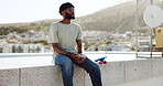 Black man, relax and rest on wall with skateboard on building rooftop in city. calm, serene and young happy trendy skater guy with phone chill freedom adventure outdoors in bokeh town background