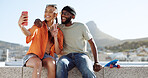 Happy, skateboard and couple taking a selfie on a phone while sitting on a rooftop in the city. Happiness, peace sign and young interracial man and woman taking photo with smartphone in a urban town.