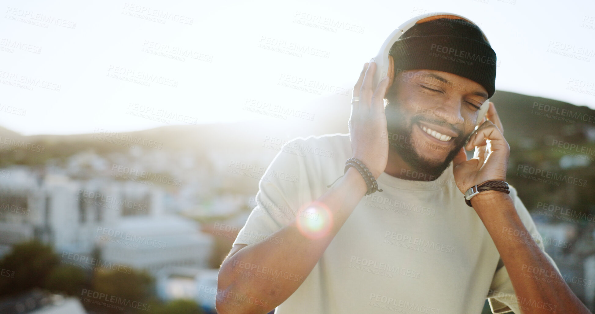 Buy stock photo Face, smile and music with a black man in the city for freedom, energy or wellness during summer. Flare, roof and headphones with a happy young person listening to the radio in an urban town