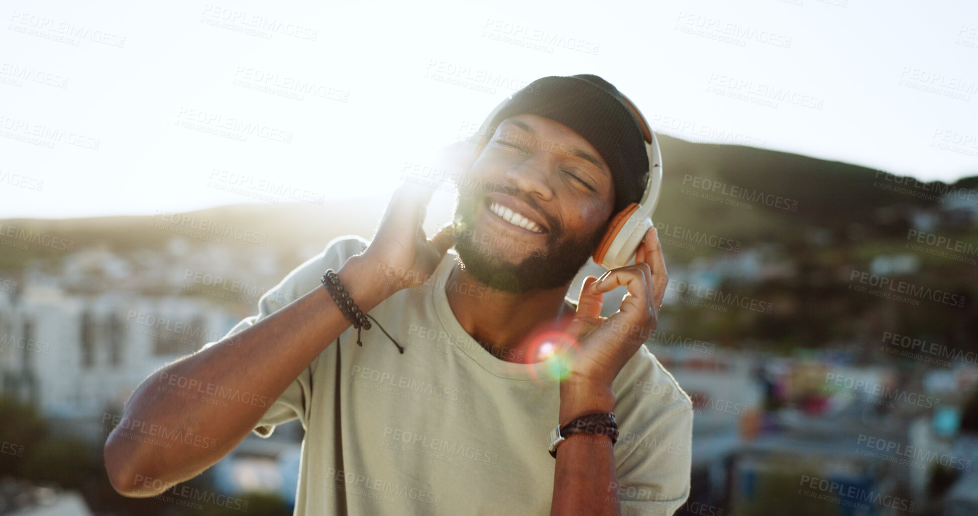 Buy stock photo Face, music and a happy black man in the city for freedom, energy or wellness during summer. Flare, smile and headphones with a happy young person listening to the radio on a roof in an urban town