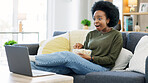 Happy african american woman streaming online movies on a laptop while snacking on popcorn and relaxing on a sofa at home. Black female enjoying a comedy, eating, laughing and having fun on a weekend