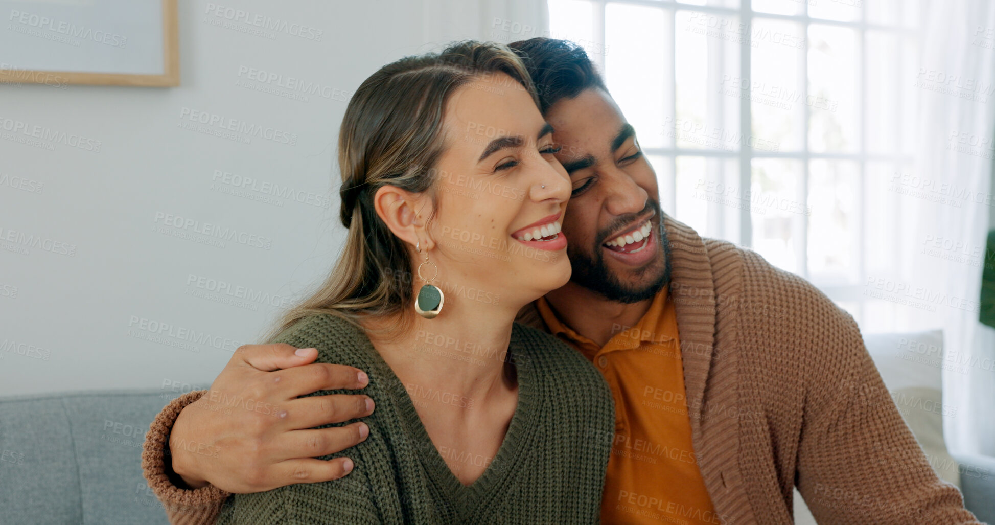 Buy stock photo Love, smile and hug with an interracial couple on a sofa in the living room of their home together for romance. Happy, funny or laughing with a man and woman in their house to relax while bonding