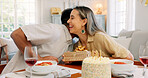 Interracial couple, gift and celebrate birthday being happy, kiss and smile in home at table with cake. Love, man and woman being content, romantic and present being cheerful celebration together.